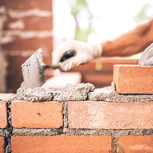 Bricklayer worker installing brick masonry on exterior wall with trowel putty knife