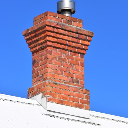 Vintage red brick chimney with modern metal lining on top of white corrugated sheet metal roof.